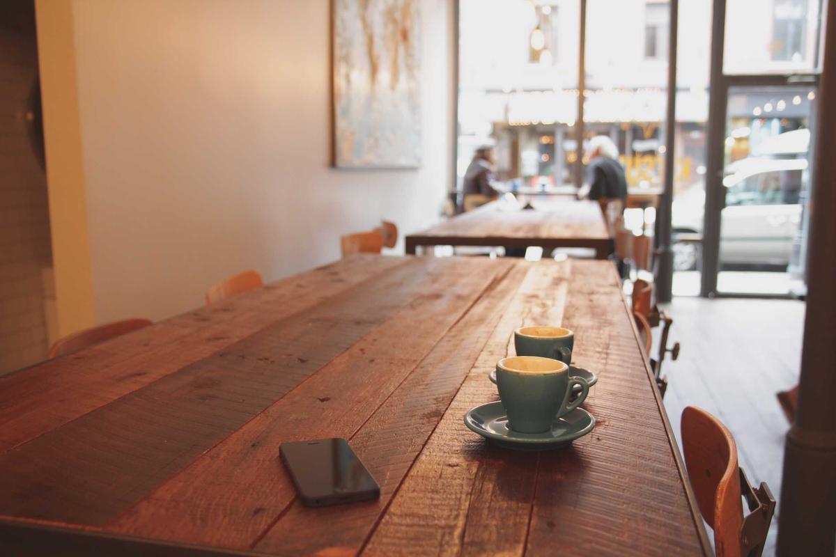 Une tasse de café sur une longue table en bois, dans un café lumineux.