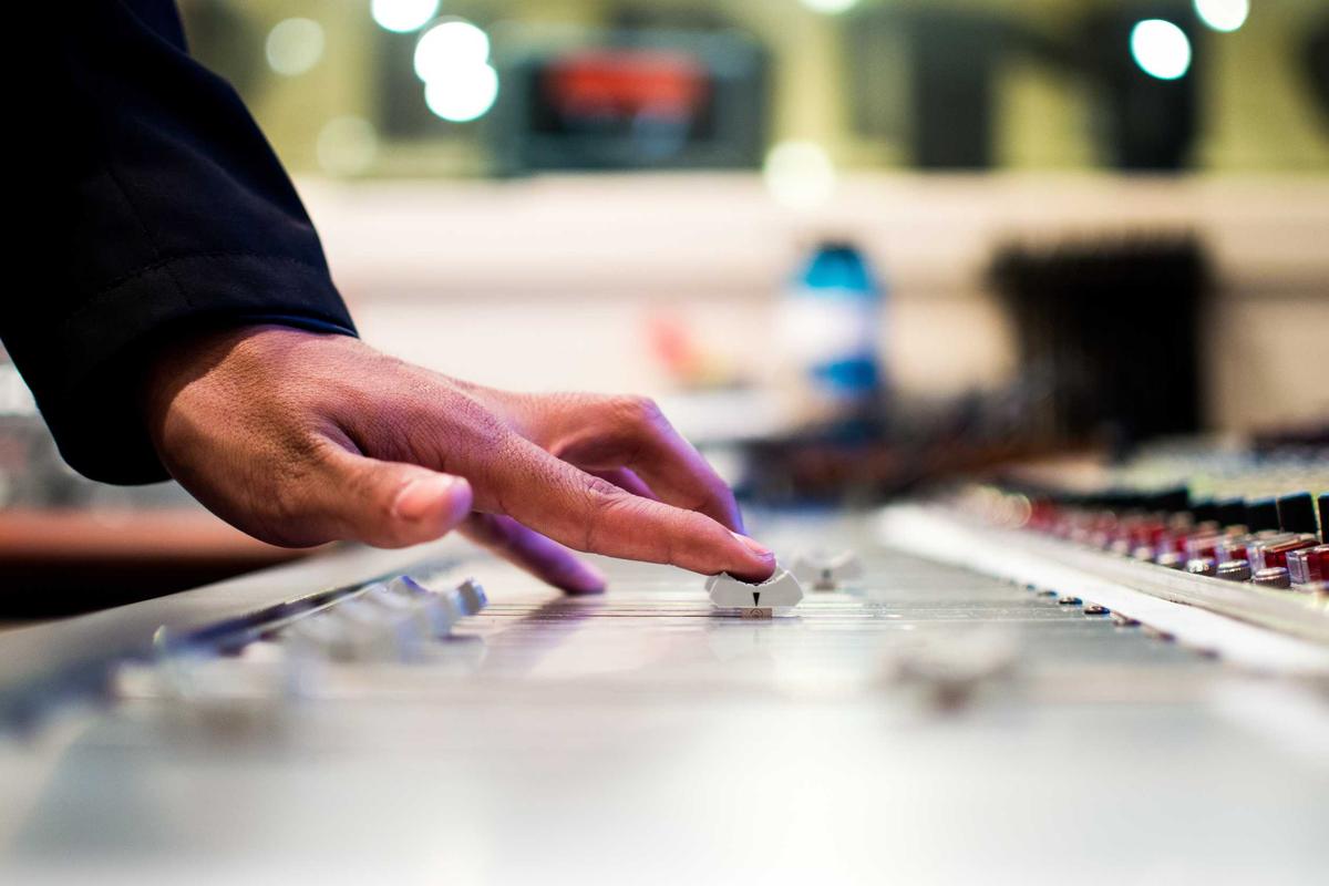 Une main règle les curseurs d'une table de mixage.